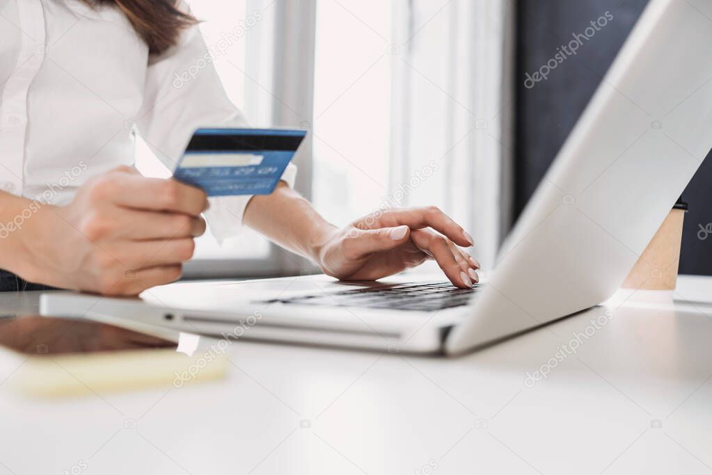 Woman hand holding credit card and using laptop at home. Businesswoman or entrepreneur working. Online shopping, e-commerce, internet banking, spending money, working from home concept