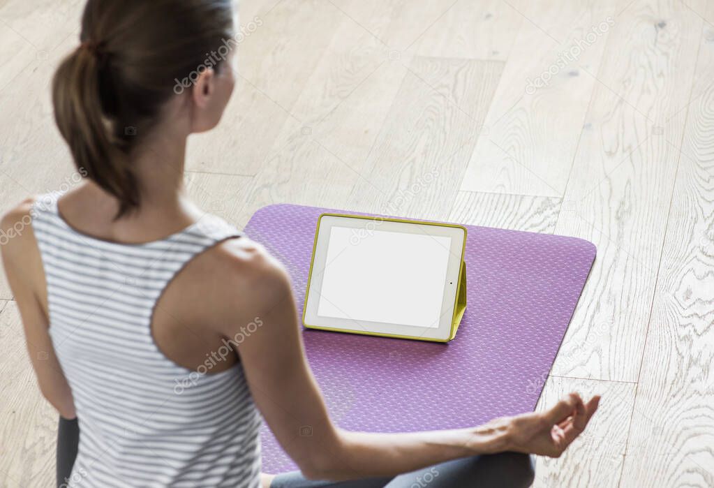 Young woman practicing yoga at home. Online video training. Girl doing exercises and meditate. Yoga, meditation, relaxation, healthy lifestyle, online training concept. Blank empty screen monitor