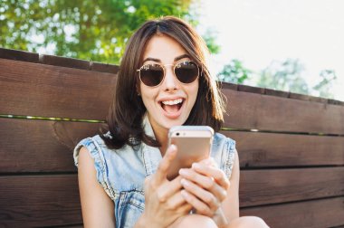 Dışarıda akıllı telefon kullanan güneş gözlüklü genç kız.