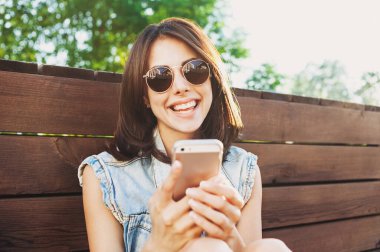 Dışarıda akıllı telefon kullanan güneş gözlüklü genç kız.
