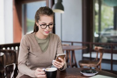 Kafede akıllı telefon kullanan güzel bir kadın. 