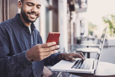 Kafede akıllı telefon ve dizüstü bilgisayar kullanan genç adam. 