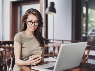 Kafede dizüstü bilgisayar ve akıllı telefon kullanan kadın. İş, teknoloji kavramı