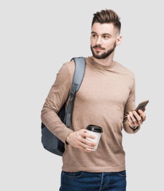 Sırt çantasında akıllı telefon ve gri arka planda izole kahve tutan yakışıklı bir delikanlı. Ciddi öğrenci ya da iş adamı portresi. Neşeli adamlar seyahate çıkıyor.