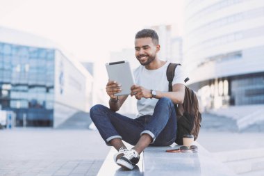 Genç yakışıklı adamlar şehirde dijital tablet kullanıyorlar. Öğrenci açık havada kitap okuyor. Kahve molası. Modern yaşam tarzı, bağlantı, iş konsepti