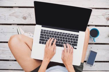 Dışarıda dizüstü bilgisayar kullanan genç bir kadın.