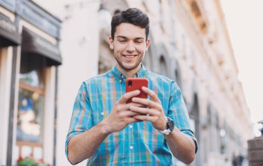 Şehirde akıllı telefon kullanan genç ve yakışıklı bir iş adamı. Cep telefonu tutan neşeli adamlar. Teknoloji, bağlantı, iletişim, sosyal medya, eğlence, iyi haber, rahatlama, eğlence kavramı