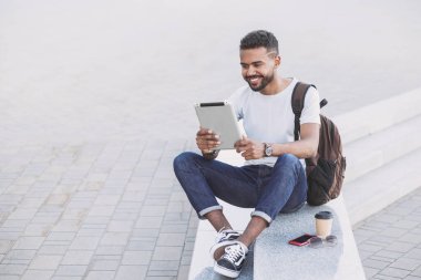 Genç yakışıklı adamlar şehirde dijital tablet kullanıyorlar. Öğrenci açık havada kitap okuyor. Kahve molası. Modern yaşam tarzı, bağlantı, iş konsepti