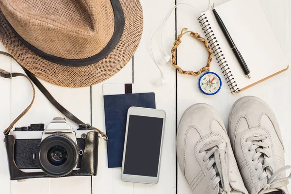 Seyahat için aksesuarlar. Ahşap arka planda farklı nesneler. Pasaport, fotoğraf makinesi, akıllı telefon, ayakkabı, güneş gözlüğü ve kitap okuyucu. Üst Manzara. Turizm, tatil ve turizm konsepti