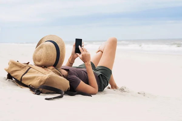 若い女性がビーチでスマートフォンで座っている リラクゼーション コミュニケーションの概念 — ストック写真