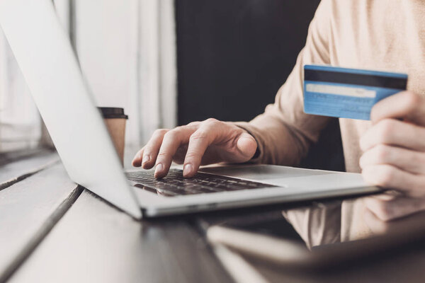 Man hand using laptop computer and holding credit card at home. Young businessman or entrepreneur working at office. Online shopping, e-commerce, internet banking, finance and freelance concept