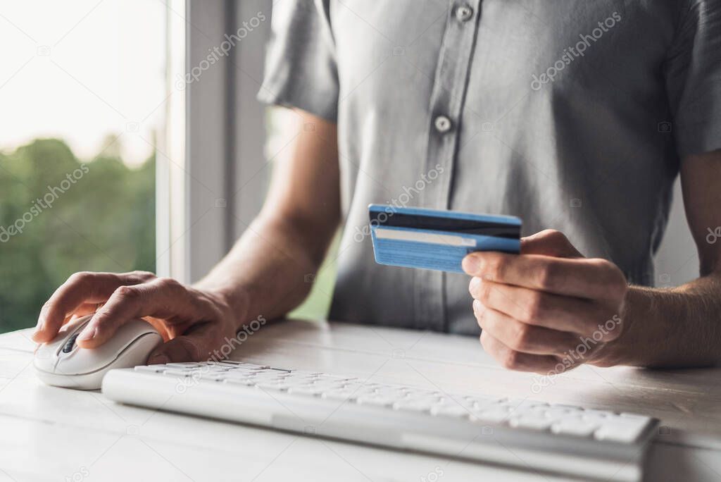 Man using computer and holding credit card. Young businessman or entrepreneur working at home. Online shopping, e-commerce, internet banking, finance and freelance concept