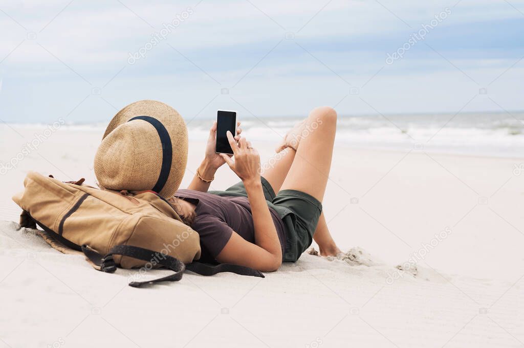 Young woman sitting with smart phone on a beach. Relaxation, travel and communication concept