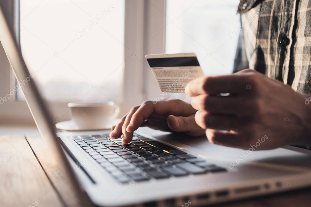 Man hand using laptop computer and holding credit card at home. Young businessman or entrepreneur working at office. Online shopping, e-commerce, internet banking, finance and freelance concept