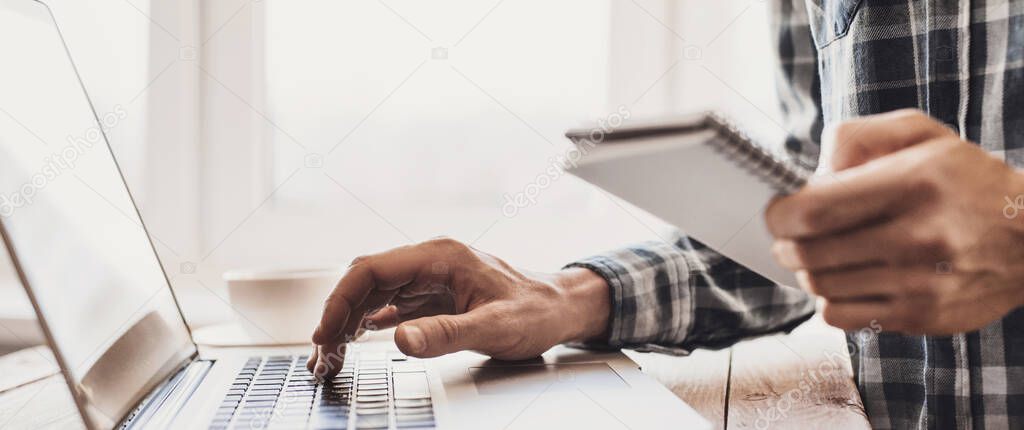Man working on computer at home. Businessman using laptop and holding notebook in office. Business, online learning, marketing, freelance, studying, distance education concept. Panoramic banner