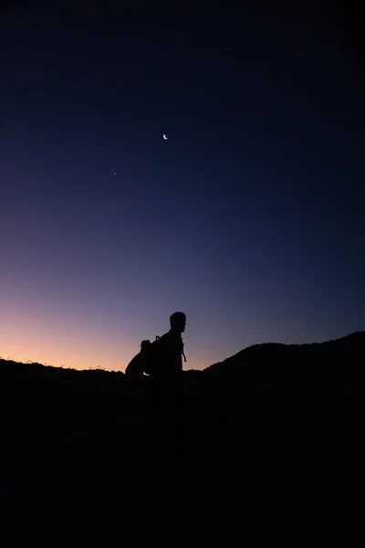 silhouettes of person and the moon in a sunrise from the mountain