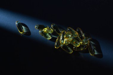 Omega-3 vitaminleri, yağ asitleri. Siyah arka planda sarı kapsüllerdeki balık yağı.