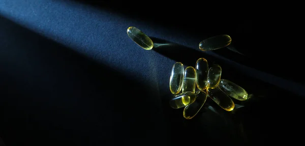 Omega-3 vitaminleri, yağ asitleri. Siyah arka planda sarı kapsüllerdeki balık yağı.