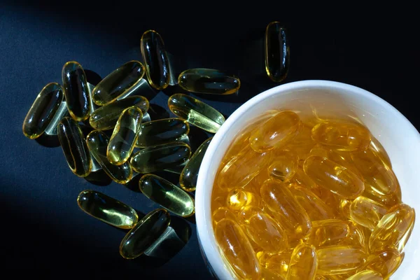 Omega-3 vitamins, fatty acids. Fish oil in yellow capsules on a black background.