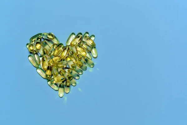 Omega-3 vitaminleri, yağ asitleri. Mavi arka planda sarı kapsüllerdeki balık yağı.