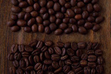 Kahve çekirdekleri koyu ahşap üzerine dökülmüş, kavrulmuş, kahverengi. Ters ve ters yönde gruplandırılmış. Gruplar arasında boşluk, koyu tahta yüzey.