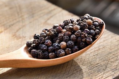 Ahşap bir kaşıkta siyah biber, ahşap bir arka plan..