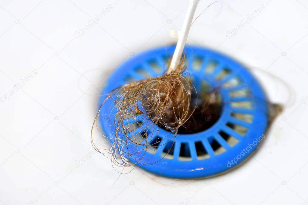 Blue plastic strainer in the sink clogged with hair, falling hair,hair in the sink wiped with a cotton swab. White porcelain background.