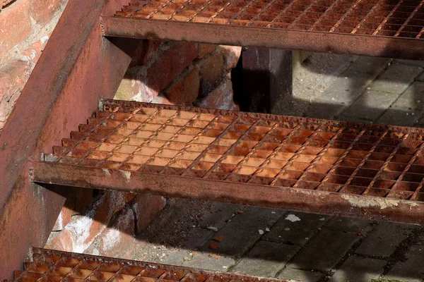 Old rusty iron stairs and brick wall. Three welded grid stairs.
