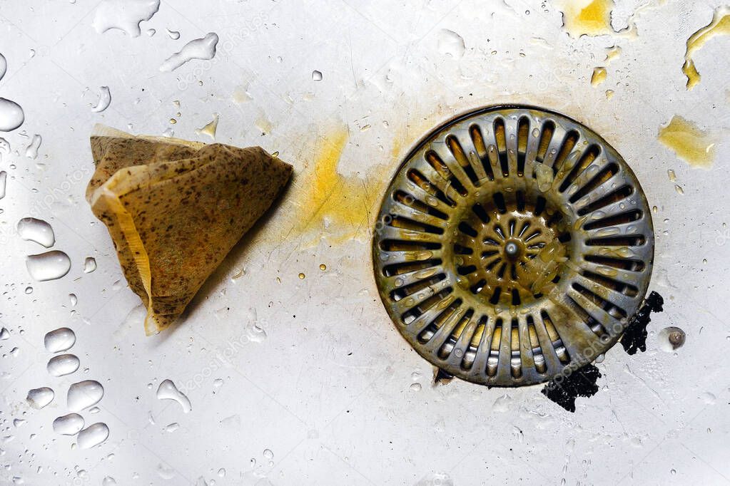 Dirty strainer in stainless steel sink, slime and dirty waste, poor kitchen hygiene. Used tea bag thrown into the sink.