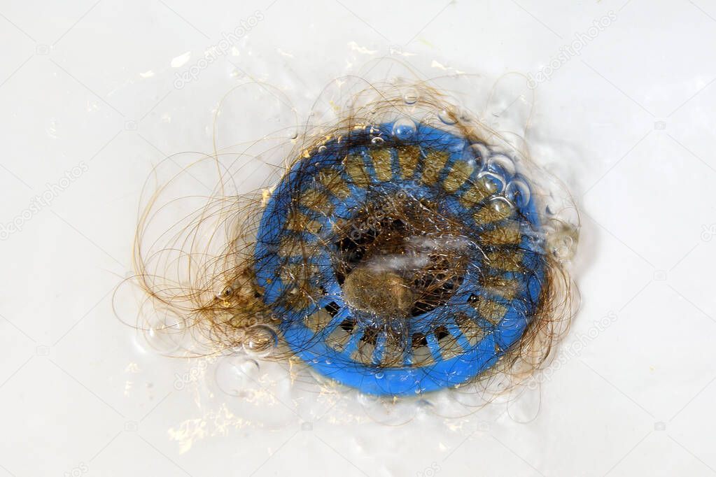 Dropped hair in a blue strainer in the sink, poor hygiene, clogged water drain. Water flows to waste.