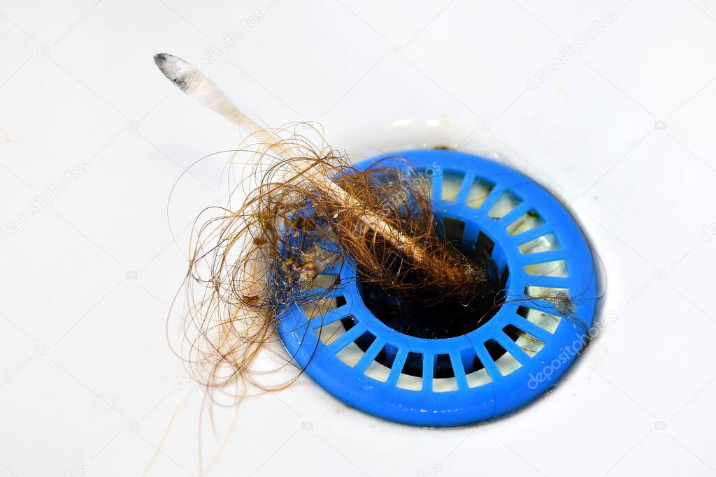 Dropped hair in a blue strainer in the sink, poor hygiene, cleaning the clogged drain with a cotton swab. Hair wrapped on a cotton bud.