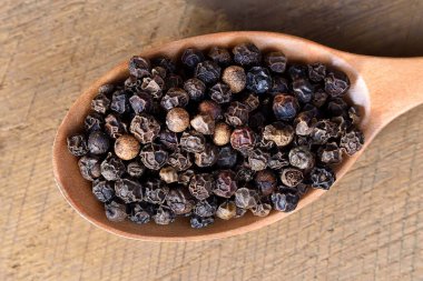 Ahşap bir kaşıkta siyah biber, ahşap bir arka plan..