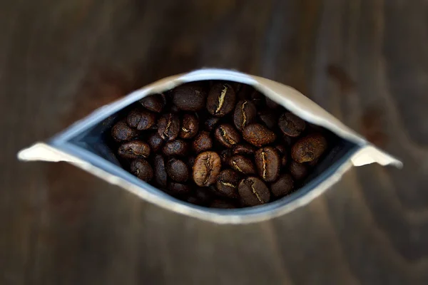 Papper coffee in bag from above with dark roasted coffee beans. Dark wooden blurred backgroung.