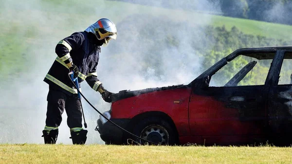 Firemen in work, car on fire. A fireman stands by the extinguished red car and opens the hood.