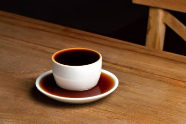 Kahveyi çay tabağıyla dolu beyaz porselen bardağa döküyorum. Dolu bir fincan kahve. Bir fincan dolusu kahve ahşap masada fincanın altına kahve dökülmüş..