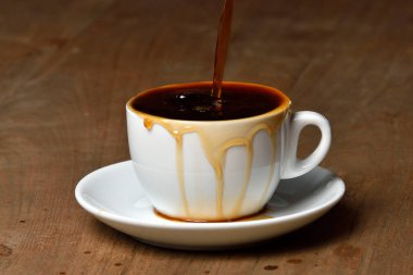 Kahveyi çay tabağıyla dolu beyaz porselen bardağa döküyorum. Dolu bir fincan kahve. Ahşap sehpanın üzerinde bir fincan kahve ve çaydanlığın suyu. Fincan kupasının altına kahve dökülmüş..