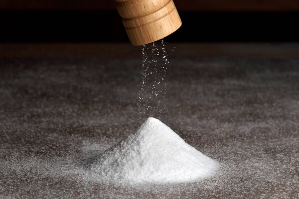 Salt grinder and pile of salt. Salt falls from the grinder on a table full of salt. Detail on grinder and pyramid of salt.