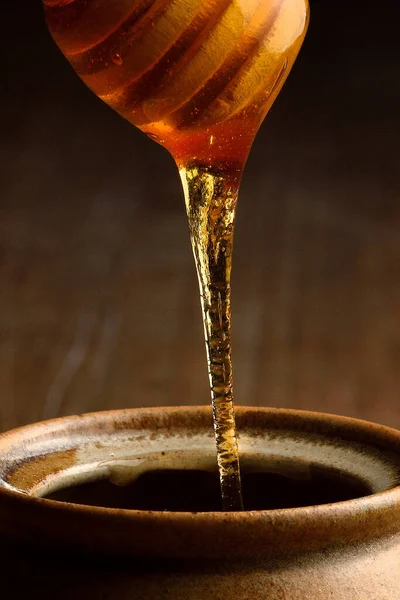 木の蜂蜜からセラミックマグカップに注ぐ蜂蜜 木製のテーブルの上に蜂蜜のための土器瓶 — ストック写真