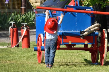 Yangın kasklı küçük bir çocuk eski bir yangın pompası makinesine ulaşmaya çalışıyor..