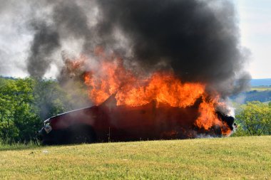 Kırmızı araba yanıyor, siyah duman. Çayırda yanan eski bir araba. Araba kazası..