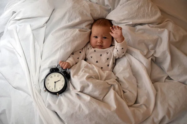 Child with an alarm clock lying on the bed, and wishes everyone a good morning. time to work. Time to sleep. Top viev — Stock Photo, Image