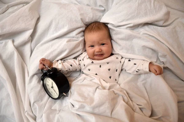 Child with an alarm clock lying on the bed, and wishes everyone a good morning. time to work. Time to sleep. Top viev — Stock Photo, Image