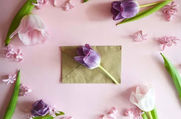 Hermosa tarjeta de felicitación floral para las vacaciones de primavera. Delicado tulipán rosa en un sobre sobre sobre un fondo rosa. Colores pastel de primavera. Vista superior — Foto de Stock