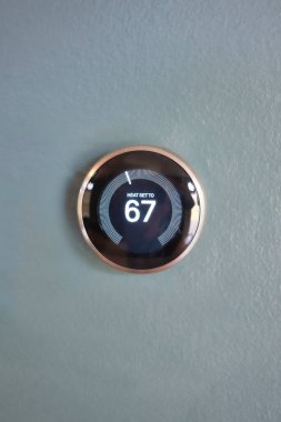 Smart thermostat isolated on light blue wall. Nest smart home technology saving money heating and cooling. Green tech saving energy clipart