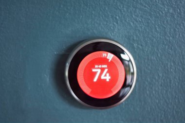 Kırmızı merkezli akıllı ev termostatı ısı modunda. Enerjiyi evi ısıtmaktan kurtarıyorum. Mavi duvarda izole edilmiş ürün
