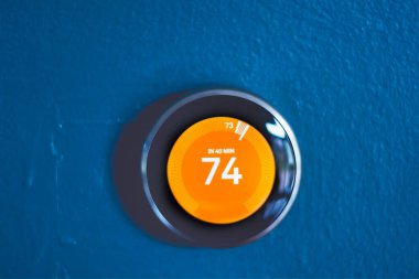 Kırmızı merkezli akıllı ev termostatı ısı modunda. Enerjiyi evi ısıtmaktan kurtarıyorum. Mavi duvarda izole edilmiş ürün