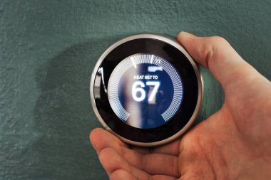 Yuva akıllı ev termostatı kullanıcı eliyle ayarlanıyor. Çevreci teknoloji ısıtma ve soğutmadan tasarruf etmek için düğmeye bas