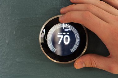 Yuva akıllı ev termostatı kullanıcı eliyle ayarlanıyor. Çevreci teknoloji ısıtma ve soğutmadan tasarruf etmek için düğmeye bas