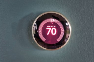 Mavi duvarda kırmızı merkez bilgisi olan akıllı ev termostatı. Ev ısısını 70 dereceye çıkarıyorum..