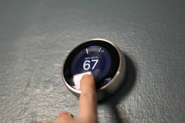 Hand adjusting the dial on smart home thermostat. Pressing center button to save money heating and cooling.